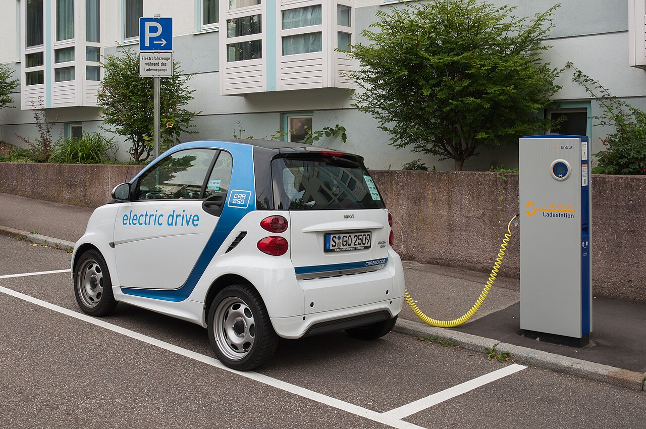 Small two-seater electric car connected to a kerbside charging post in a city street