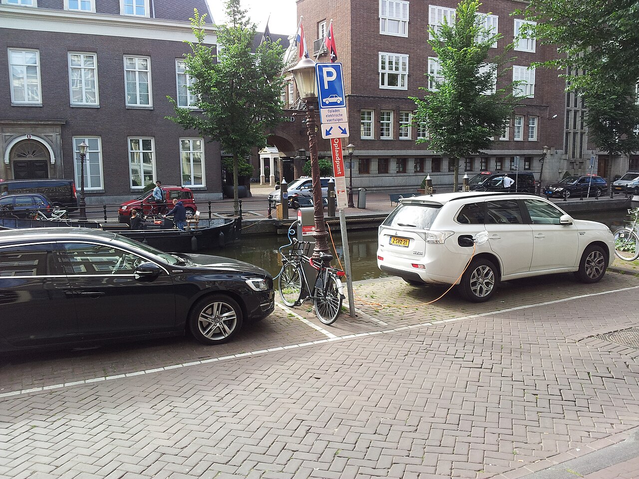 Two plug-in cars charging from a shared post beside an Amsterdam canal
