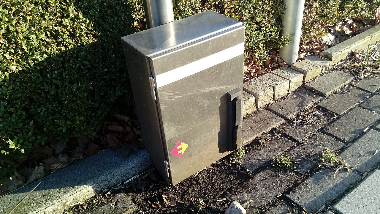 Charging post on a paved verge in a Dutch village, with houses behind