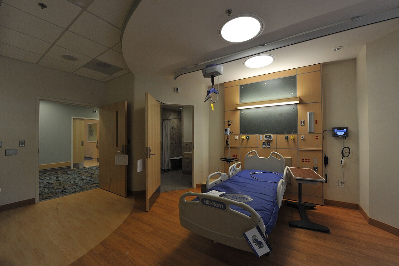 Interior of an unoccupied inpatient room with bed, ceiling lift track and seating
