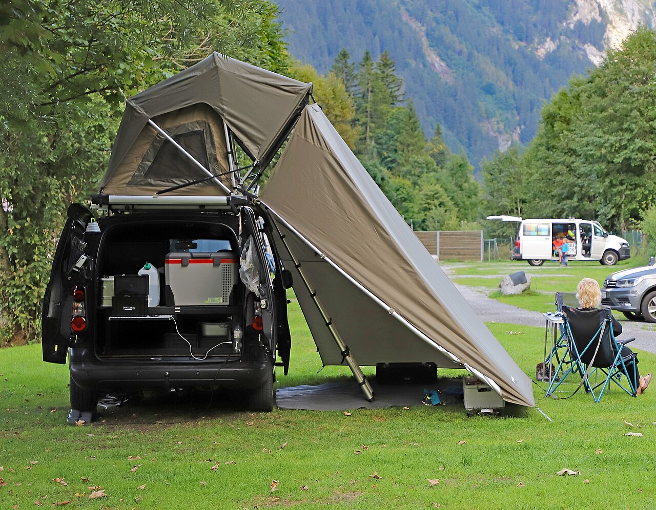 Roof tent erected above a car parked on grass