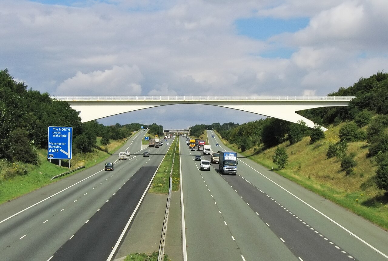 Three-lane British motorway with traffic in both directions under a grey sky