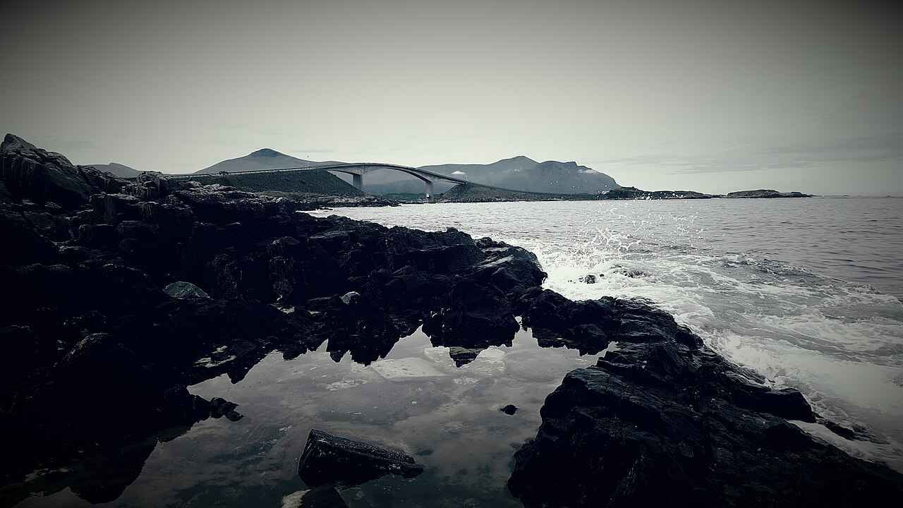 Curved bridge carrying a road between low rocky islets on the Norwegian coast