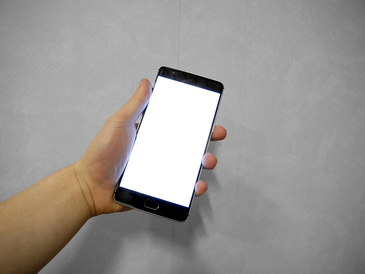 Hand holding a smartphone whose screen is entirely blank and white